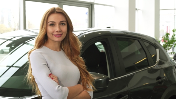 Young Beautiful Woman Smiling To the Camera Standing at the Car Dealership