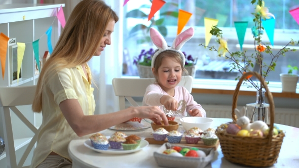 Young Mother and Her Little Daughter with Rabbit Ears Cooking Easter Cupcakes