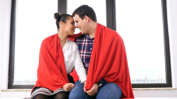 Romantic Couple Covered with a Blanket Next To a Big Window