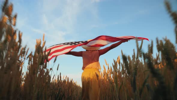 Young Woman with the USA Flag in Her Hands Walking Across the Field