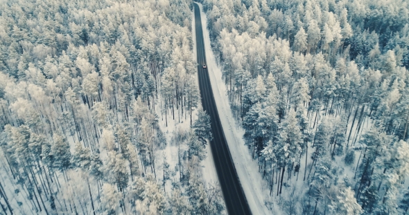 Aerial View of a Car Driving on a Snowy Forest Road