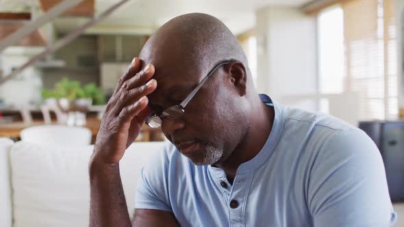 African american senior man sitting on a couch rubbing his forehead in thought