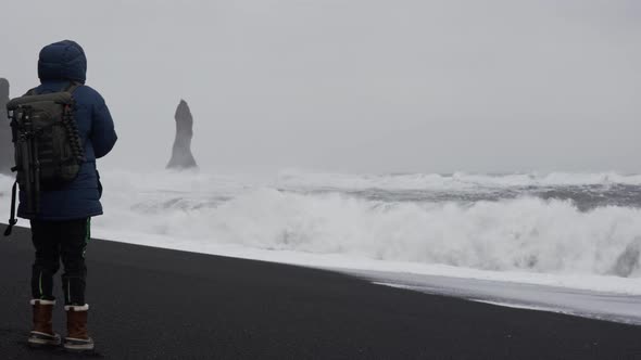 Photographer Standing On Black Sand Beach With White Sea