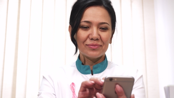 Asian Female Doctor Using Her Smart Phone at Work Smilin Cheerfully