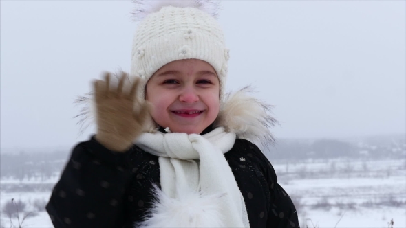 A Little Girl at the Age of 5 in the Winter, It's Snowing on the Street, She Looks at the Camera