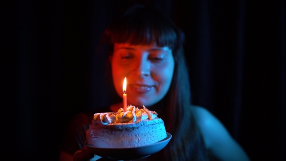 Woman Blowing Out a Candle on a Cake on a Black Background