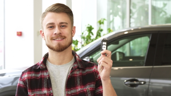 Attractive Young Man Smiling Holding Car Keys Posing at the Automotive Dealership