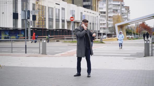 Handsome man in coat talks the phone outdoors.