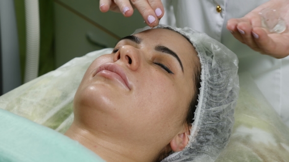 Beauty Clinic Concept.  of Beautician Spreading Cream Before Facial Procedure. Young Woman . Facia