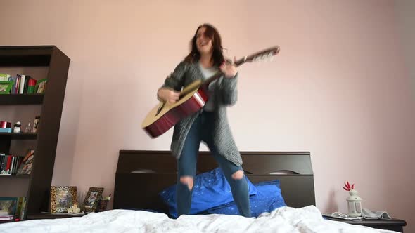 Young beautiful eastern woman jumping on her bed playing guitar