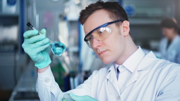 Young Scientist Checking Test Tubes in the Lab. Man Wears Protective Goggles