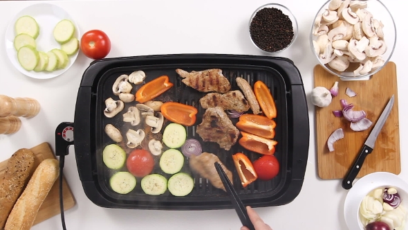 Cook Preparing Pork Meat and Vegetables on a Grill in the Kitchen