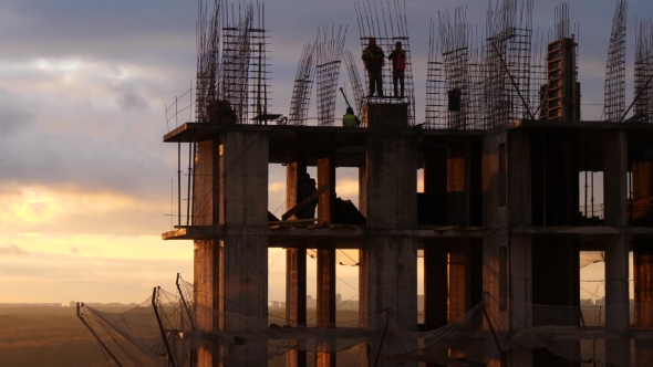 Costruction Site Against Cloudy Sunset Sky. Workers Among Rebar Rods and Concrete Frames