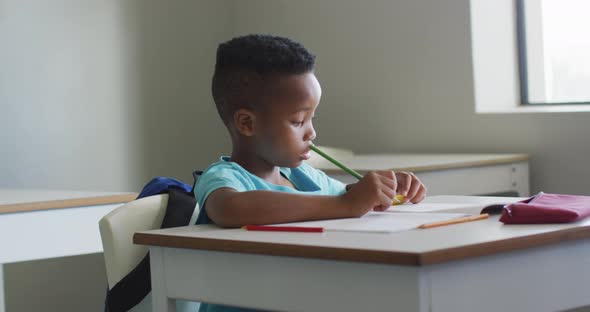 Video of african american boy sitting at desk during lesson in classroom