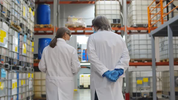 Back View of Specialists in Lab Coat and Gloves Walking in Industrial Warehouse