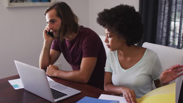 Mixed race couple calculating finances and talking on smartphone at home