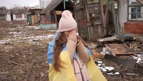 a girl wearing in the Ukrainian flag is crying against the background of destroyed houses. War in Uk