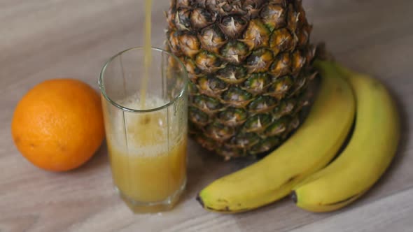 A Man Pours Pineapple Juice in a Glass on a Wooden Background