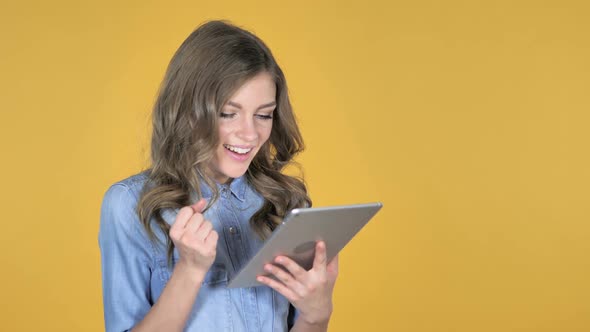 Young Girl Excited for Success While Using Tablet Isolated on Yellow Background