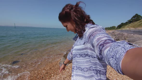 POV Shot Of Young Woman Reaching Down To Pick Up Plastic Bottle On Beach In Slowmotion