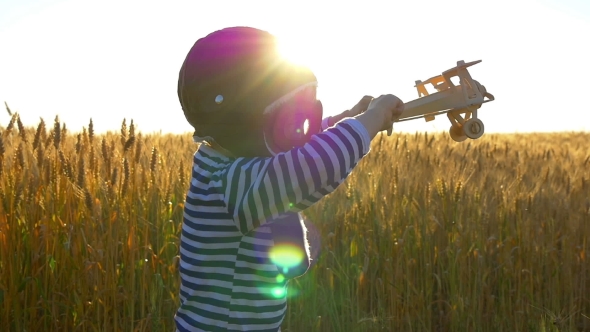 Happy Child Playing with a Toy Airplane at Sunset in a Wheat Field