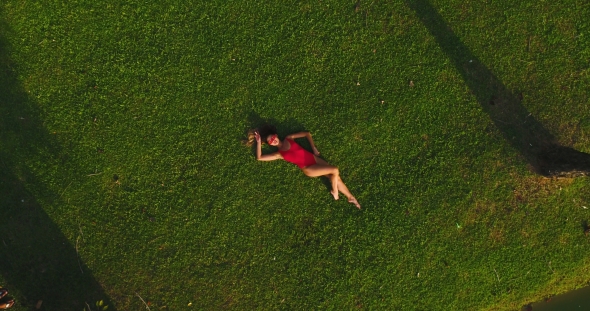 Aerial: Attractive Girl Lies on the Green Grass and Posing on the Camera.