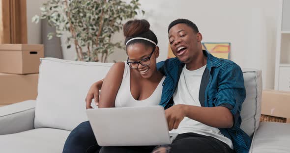 A Man Embraces His Woman While Sitting Relaxing on the Couch They Hold a Laptop on Their Lap Watch a