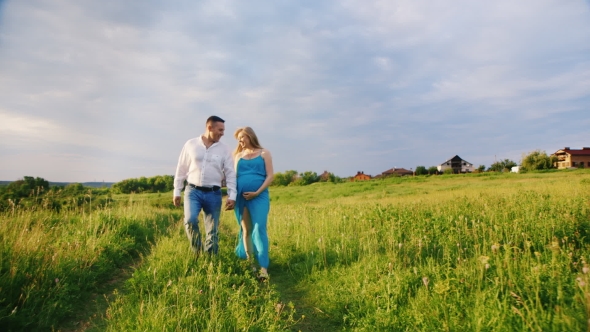 Young Couple - Husband and Pregnant Wife Are Going Through the Countryside at Sunset