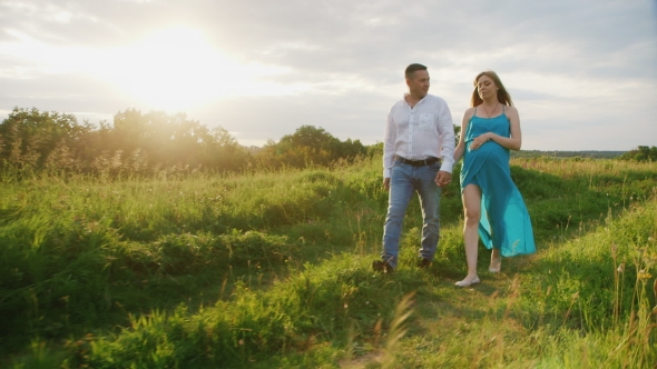 Steadicam Shot: Young Couple - Husband and Pregnant Wife Are Going Through the Countryside at Sunset