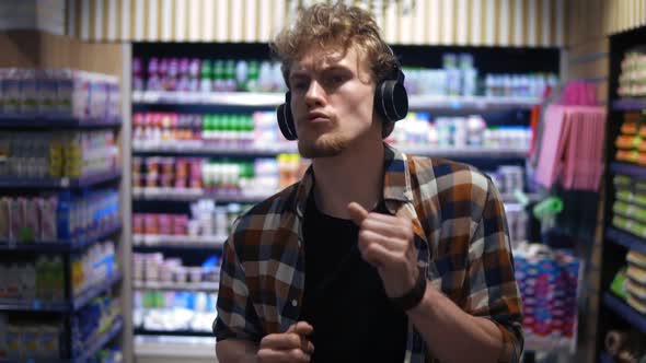 At the Supermarket Stylish Caucasian Guy with Headphones Walks Through Goods Section of the Store