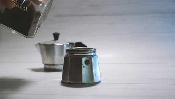 A wooden spoon pours freshly ground coffee into a geyser coffee maker