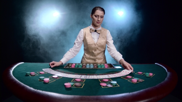 Girl Croupier at a Casino Shuffles Cards on Black Smoky Background with Spotlights.