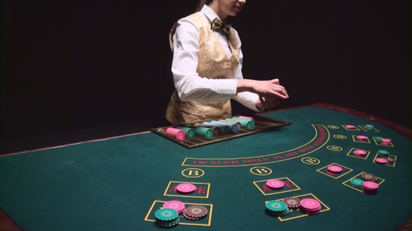 Casino Female Croupier Distributes Cards on the Poker Table Top Using Cut Card. Black Background.