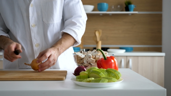 Cook in Modern Kitchen Cuts Onion on Wooden Table