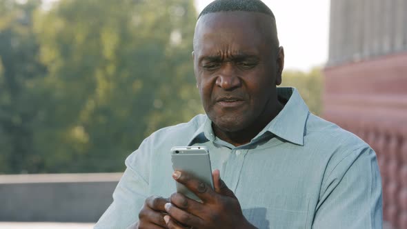 Mad Stressed African Man Holding Cellphone Annoyed with Mobile App Error Spam Message on Slow Stuck