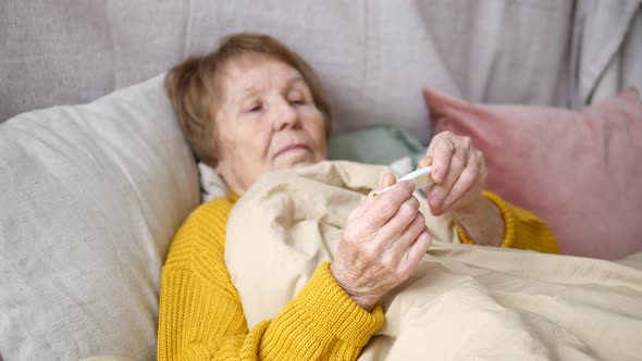 Elderly Woman Checking Temperature On Thermometer Lying In Bed