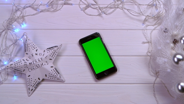 Mobile Phone Lies on a White Table, Next To Christmas Toys and Garlands. Top View