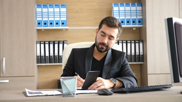Young Businessman in His Office Taking Notes in a Paper Notebook