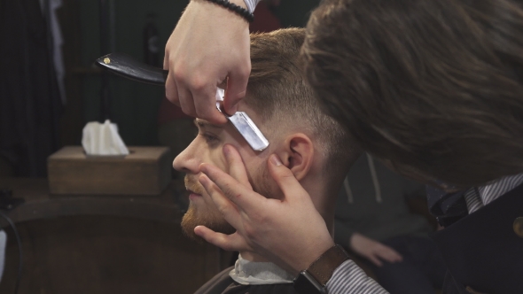 of a Handsome Man Getting Shaved with a Razor By a Barber