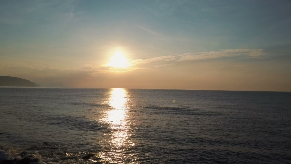 Slow Flight Above Small Waves Facing Beautiful Sunrise and Mountains on Horizon. Aerial Drone Shot