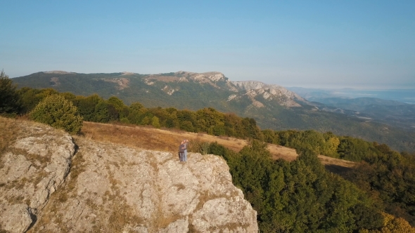 Aerial Flight Over Young Couple Standing on Cliff Edge 