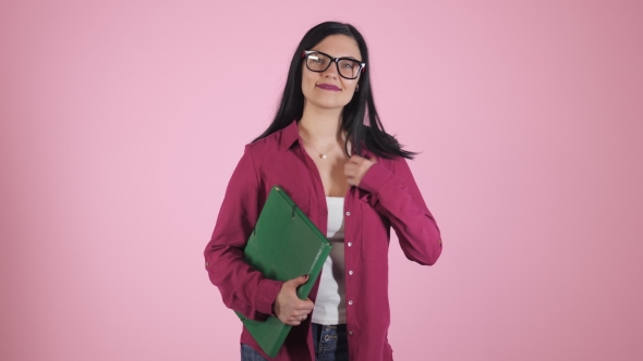 Young Caucasian Brunette Haired Teenage Girl in Glasses with Big Green Folder Smiling on Pink