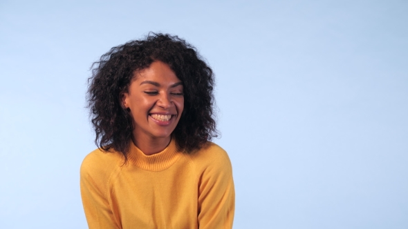Cute African Girl in Yellow Sweater on Blue Background in the Studio. The Woman Laughs Sincerely