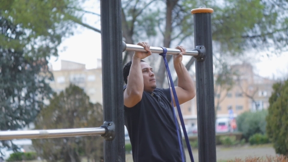 Street Workout Training. Cross Fit Man Doing Pull-ups with Resistance Band on Outdoor Gym in the