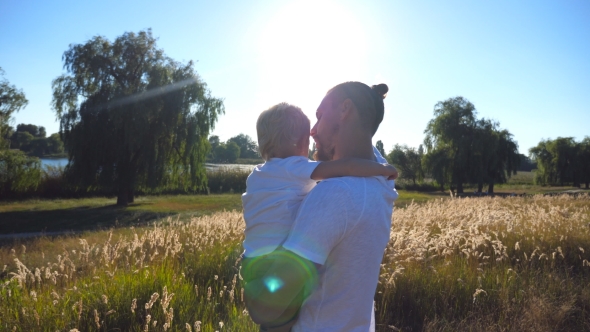 Young Dad Holding His Son on Hands at the Meadow and Talking Something to Him