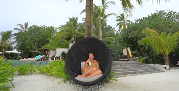 Girl Sitting in Luxurious Hanging Chair on Tropical Island Sipping a Cocktail