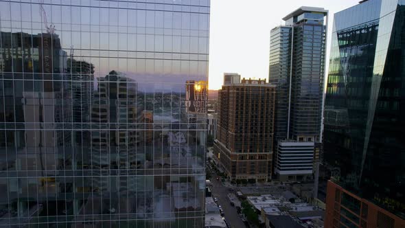 Aerial view flying in middle of mirroring highrise, revealing the 4th street and the sunset sun in A