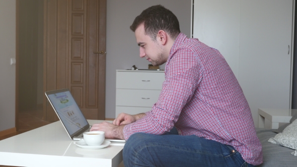 Man in Works From Home Using the Top and Trackpad. Young Business Man Sitting at Table Drinking