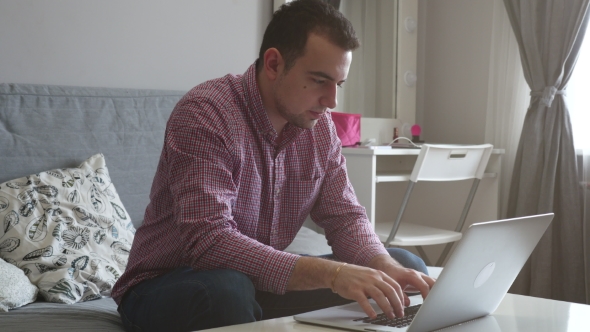 A Person Works From Home Using the Top and Trackpad. Young Business Man Sitting at Table Drinking