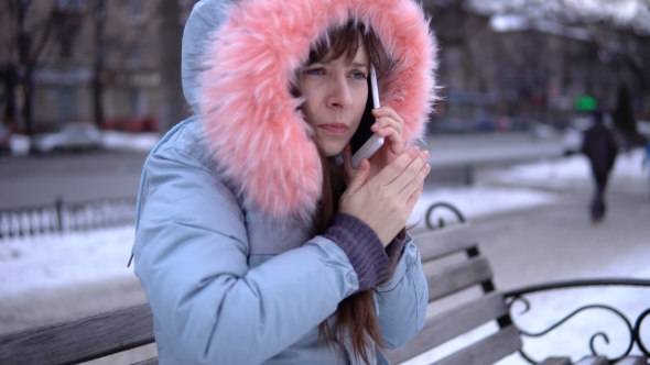 A Young Woman in a Gray Warm Jacket Uses a Phone in the Street in the Winter